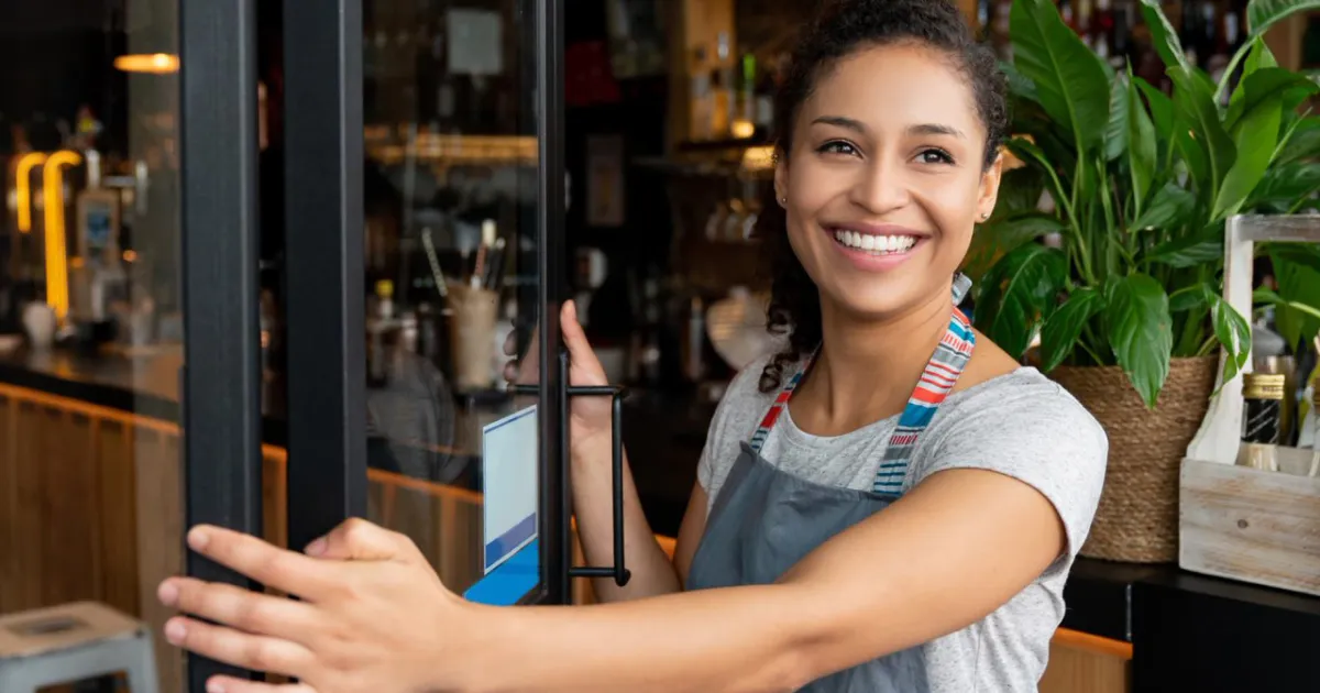 A smiling woman opens the door to a business.