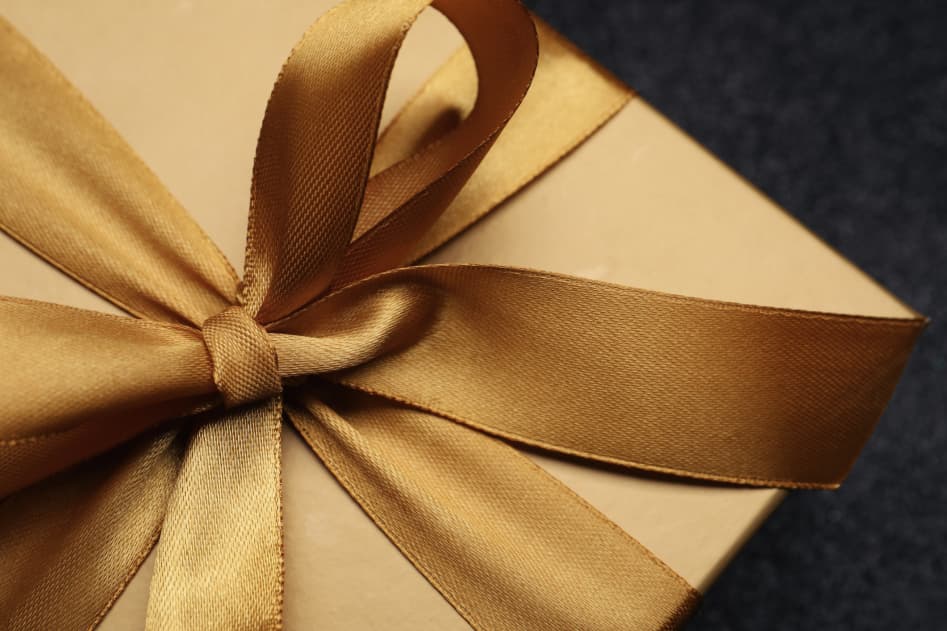 Gift box wrapped with gold wrapping paper and a large gold bow.