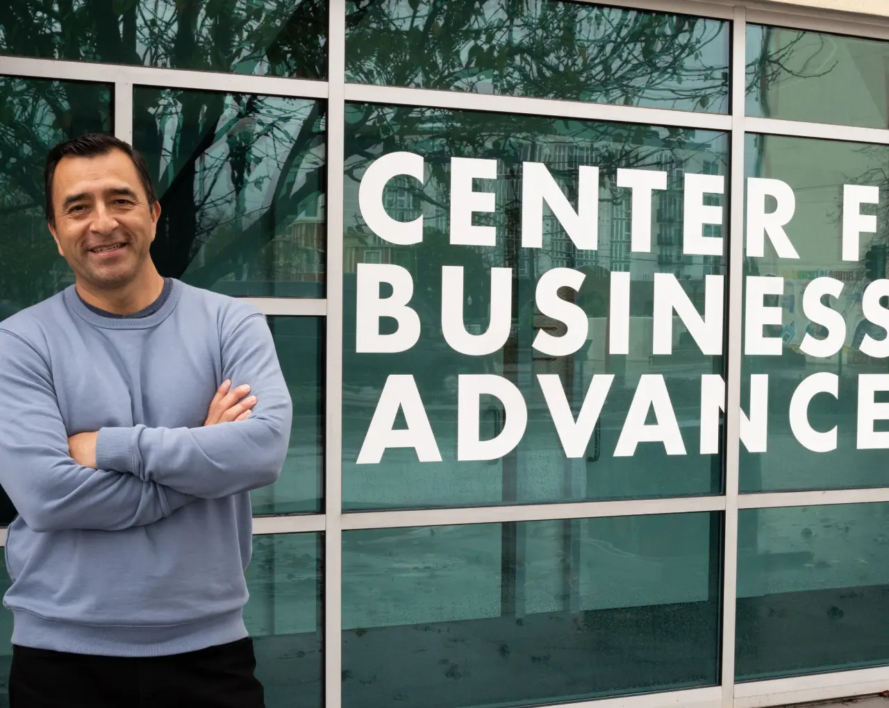 A smiling Joel Sedeño poses in front of the SBDC office, representing small business support.