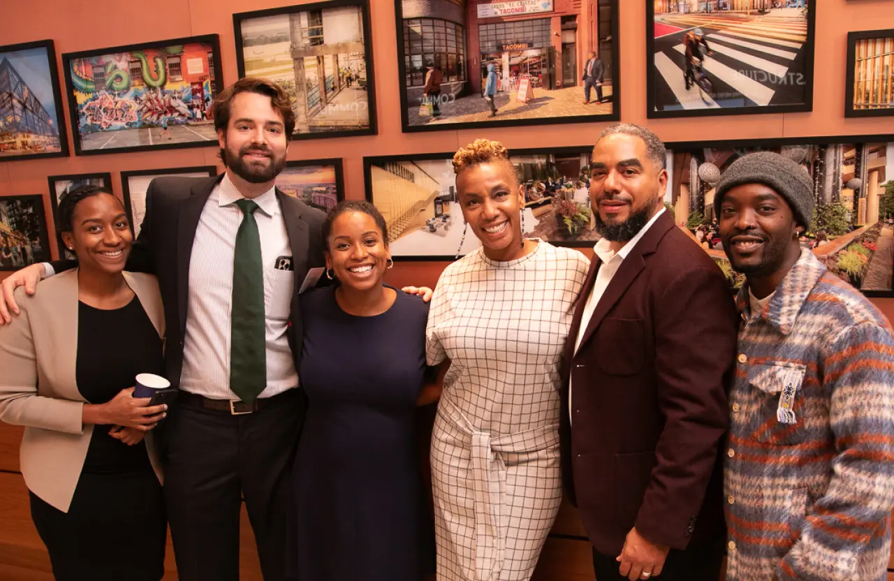 Members of Momentus Capital and Capital Impact Partner's real estate developer training program gather together in front of a wall of photos.