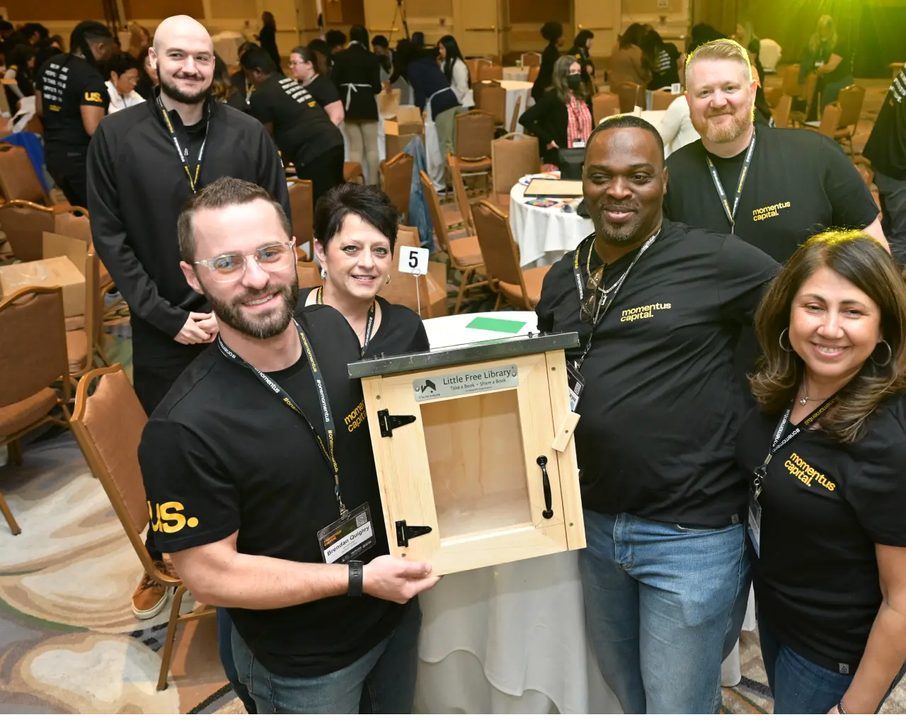Employees of Momentus Capital proudly display their completed Little Free Library during a company event.