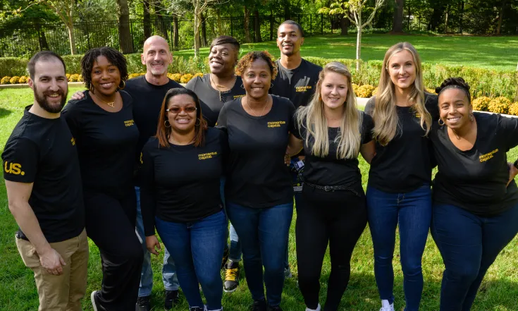 Th Human Resources team gathers together at a company event, all wearing the same t-shirt and smiling.