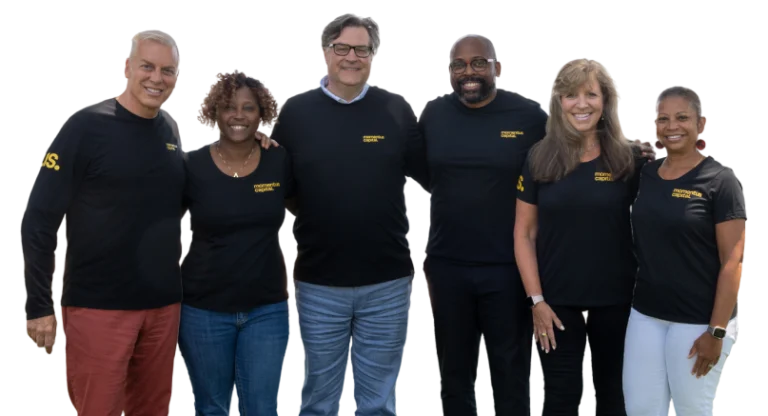 The Momentus Capital Capital Impact Partners Executive Management team gathers together at a company event, all wearing the same t-shirt and smiling (transparent background).