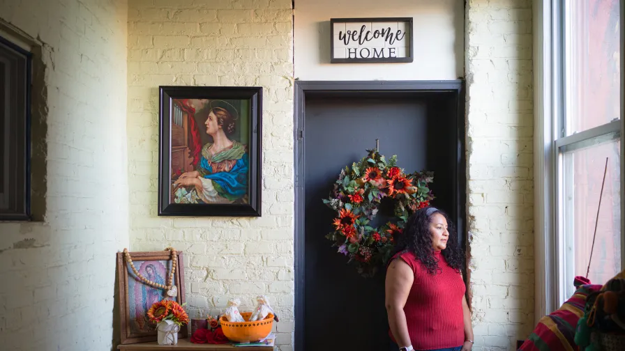 Karen Leon, an owner of Pilsen Housing co-op, wearing red, standing under a sign that reads welcome home.