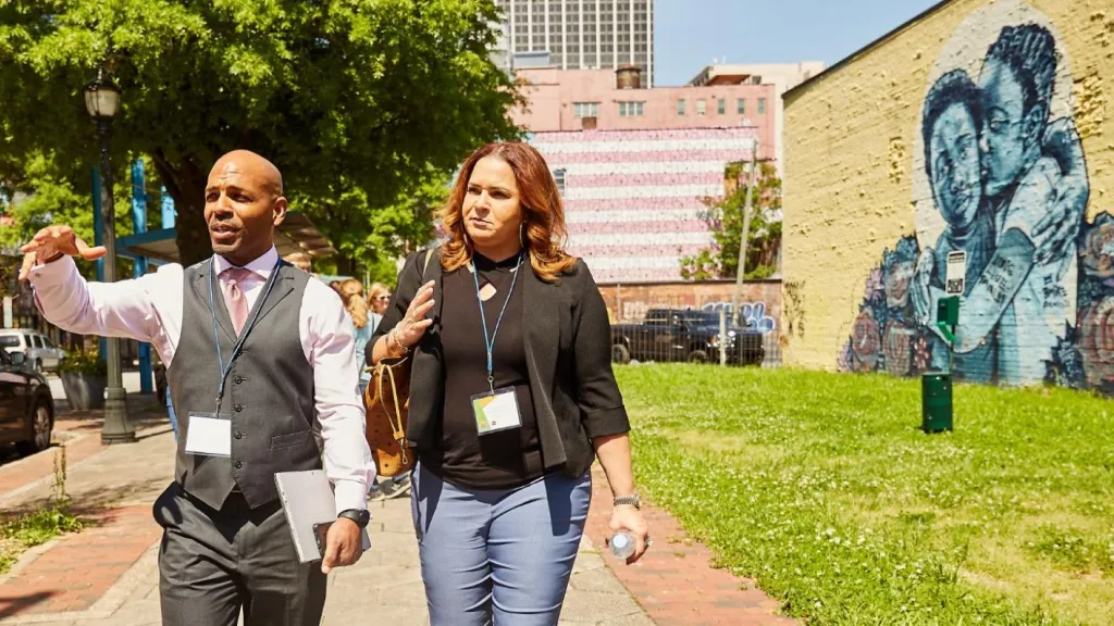 A professional man and a woman walking in a neighborhood and pointing