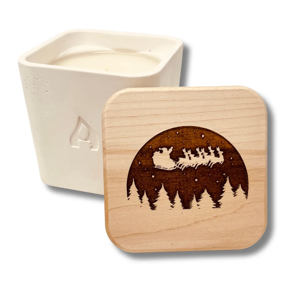 An Amador Candle in its signature, rounded square candle jar with a maple lid and a custom engraving of a Santa’s sleigh flying over pine trees featured in the Momentus Capital holiday gift guide to support small businesses as a home and decor gift.