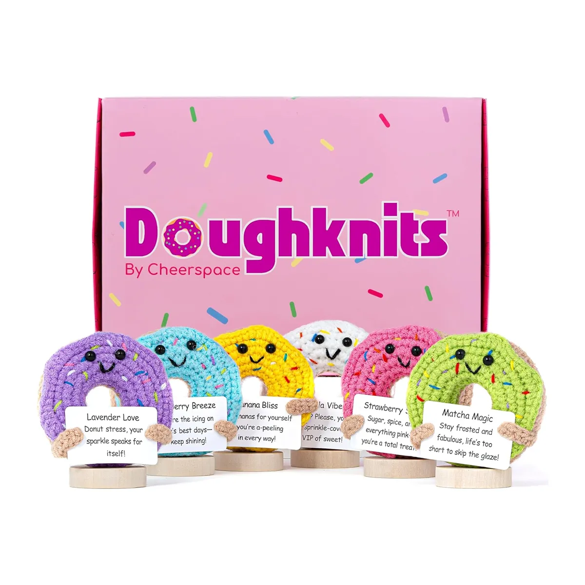 Five Cheerspace handmade crocheted donuts holding encouraging signs in front of a pink donut box featured in the Momentus Capital holiday gift guide to support small businesses as a home and decor gift.