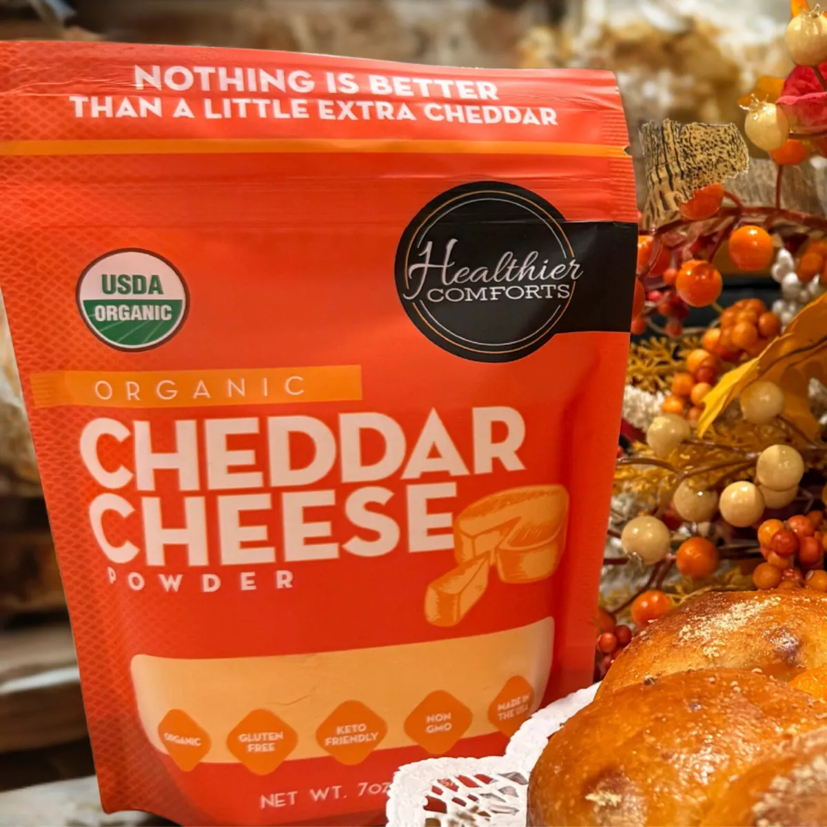 Healthier Comforts organic cheddar cheese powder photographed with simple kitchen ingredients, included as a gourmet food gift in the Momentus Capital small business gift guide.