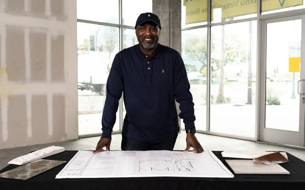 A man stands in front of a table, examining construction plans spread out before him.