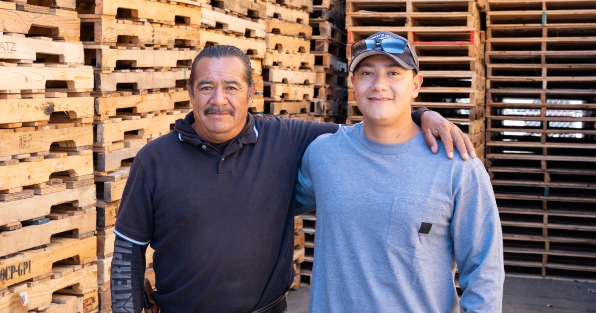 Multi-generational business owners stand arm in arm in their warehouse space.
